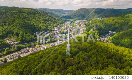 Aerial view of communication tower above forested valley and small German town with river and hills under cloudy sky 140103020