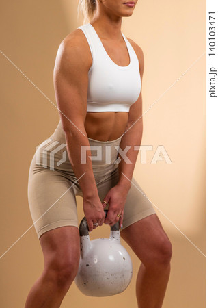 Athletic woman lifting a white kettlebell during a strength training workout in a studio setting 140103471