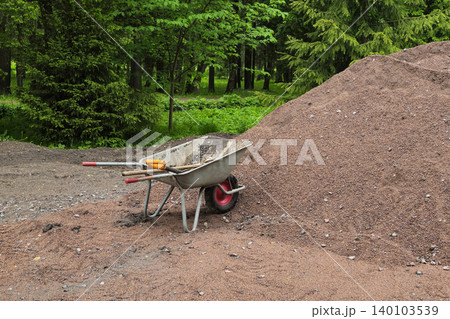 Metal wheelbarrow rests beside a pile of crushed red mulch 140103539
