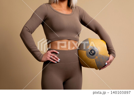 Fit woman in brown workout clothes holding a yellow medicine ball Fit woman in brown workout clothes holding a yellow medicine ball 140103897
