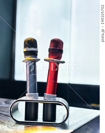 Two colorful wireless karaoke microphones in a modern charging stand, isolated on a sleek tabletop with soft studio lighting. Two colorful wireless karaoke microphones in a modern charging stand, isolated on a sleek tabletop with soft studio lighting. 140105702