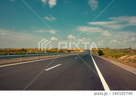 Empty highway leading through flat countryside under bright blue sky Empty highway leading through flat countryside under bright blue sky 140105740