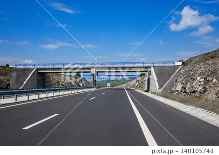 Modern highway stretches forward under bright blue sky Modern highway stretches forward under bright blue sky 140105748