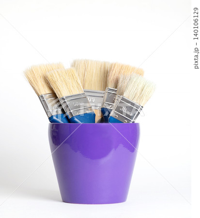Flat brushes with natural light bristles in a purple flower pot. Five thick brushes of varying widths, placed in a flower pot with the brush tip pointing upwards. Front view on white background. Photo 140106129