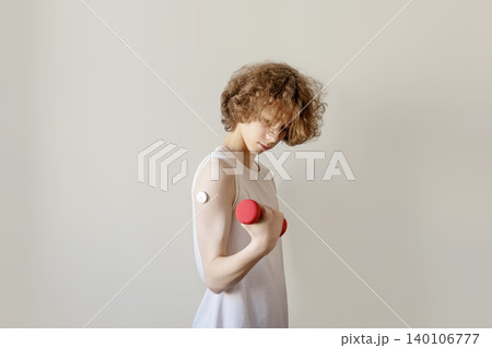 Teenage Boy with Glucose Monitor Training with Red Dumbbell on Grey Background Teenage Boy with Glucose Monitor Training with Red Dumbbell on Grey Background 140106777