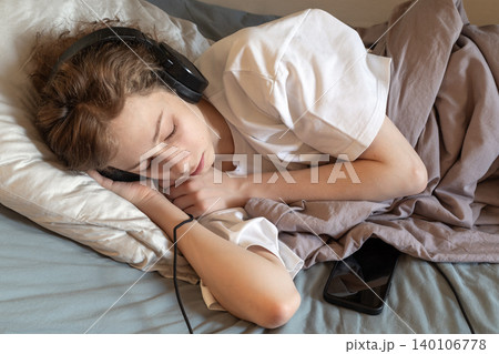 Tired Teenage Boy Sleeping in Headphones with Smartphone on Bed 140106778