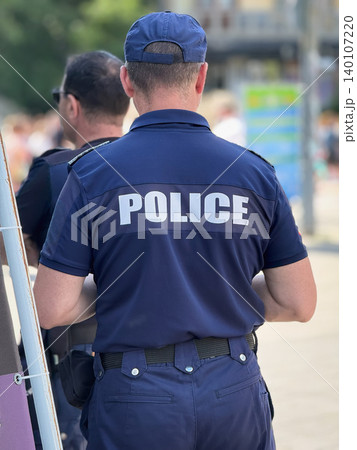 Police officer stands with back to camera during public patrol in urban street. Concept of police presence, law enforcement, security, crowd control, public safety, community protection Police officer stands with back to camera during public patrol in urban street. Concept of police presence, law enforcement, security, crowd control, public safety, community protection 140107220