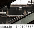 Concrete decay meets modern art in a silent, abandoned space. Neglect is disrupted by a sudden glimmer of life. Weathered concrete and rusted girders frame the hollow interior. A broken escalator cuts 140107337