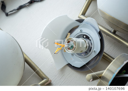 Broken glass lamp shade on a ceiling chandelier with exposed wires and internal light socket Broken glass lamp shade on a ceiling chandelier with exposed wires and internal light socket 140107696