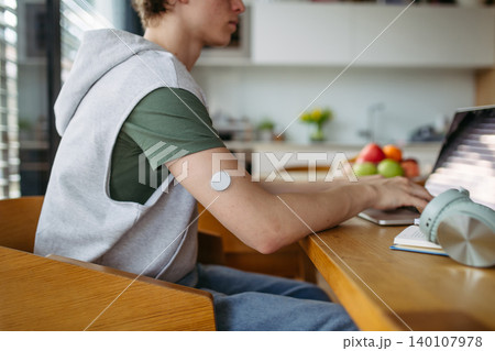 Teen boy with diabetes working on school project on laptop at kitchen table. Teen boy with diabetes working on school project on laptop at kitchen table. 140107978