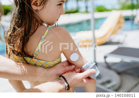 Mother changing glucose sensor for diabetic daughter by pool. Mother changing glucose sensor for diabetic daughter by pool. 140108011