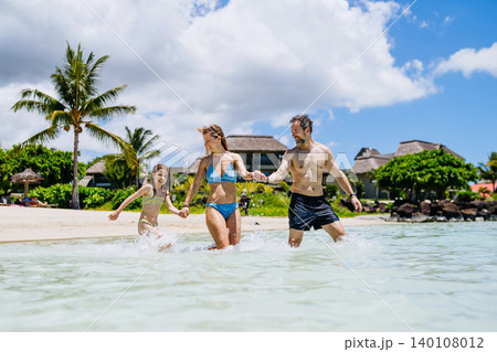 Happy family with daughter playing together in shallow tropical sea water during summer vacation. Happy family with daughter playing together in shallow tropical sea water during summer vacation. 140108012