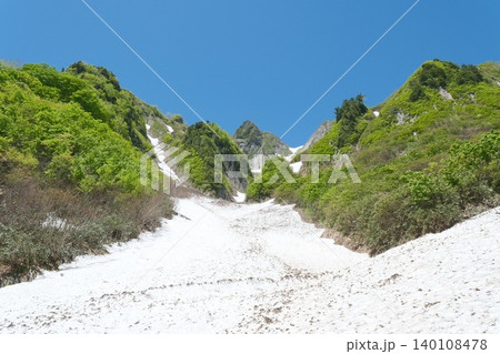 残雪の斜面越しに新緑の山肌と青空が広がる初夏の山岳風景 残雪の斜面越しに新緑の山肌と青空が広がる初夏の山岳風景 140108478