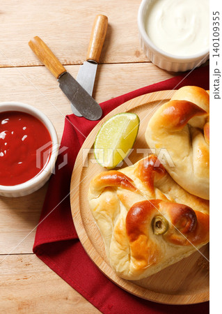A traditional baked savory closed esfiha with olives, lemon, ketchup, and olive oil, served on a round wooden plate with a red napkin 140109355
