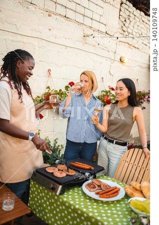 Diverse women friends enjoying summer barbecue party with wine Diverse women friends enjoying summer barbecue party with wine 140109748