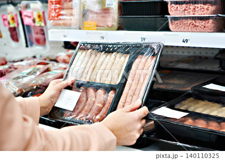 Woman chooses sausages in vacuum package at store Woman chooses sausages in vacuum package at store 140110325