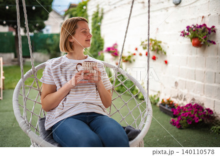 Woman relaxing in swing chair with coffee cup in garden 140110578