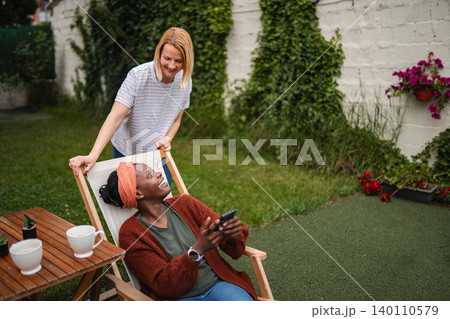 Diverse women laughing enjoying relaxing summer day in backyard Diverse women laughing enjoying relaxing summer day in backyard 140110579