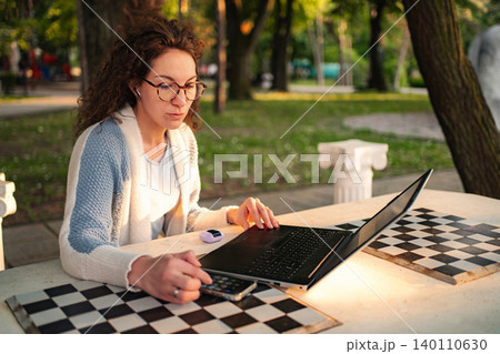 Woman working remotely on laptop outdoors in park Woman working remotely on laptop outdoors in park 140110630