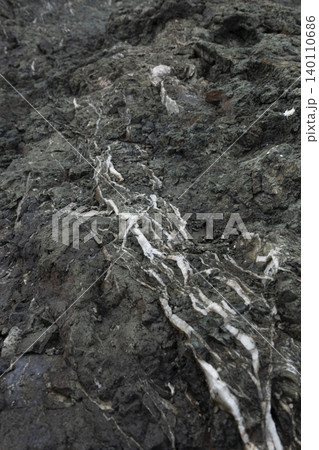 Close-up of white quartz veins branching through a dark, rugged rock surface Close-up of white quartz veins branching through a dark, rugged rock surface 140110686