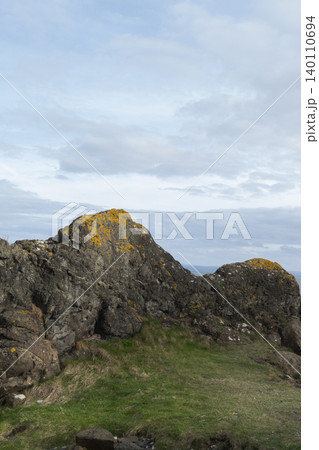 Coastal rock formation covered in patches of vibrant yellow lichen, standing against a moody, cloudy sky Coastal rock formation covered in patches of vibrant yellow lichen, standing against a moody, cloudy sky 140110694