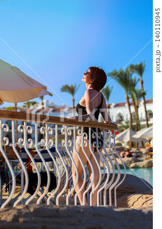 A woman in a bikini sunbathes on a bright sunny day on the hotel grounds A woman in a bikini sunbathes on a bright sunny day on the hotel grounds 140110945