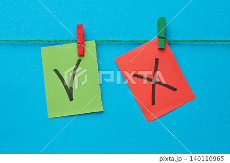 A green sticker with a check mark and a red sticker with a cross are attached to a string with wooden clothespins 140110965