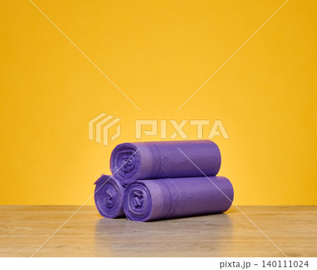 Three rolls of purple garbage bags stacked in a pyramid on a wooden surface Three rolls of purple garbage bags stacked in a pyramid on a wooden surface 140111024