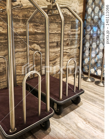 Two metallic luggage carts with purple fabric bases positioned on a polished marble floor near a decorative wall with hexagonal patterns Two metallic luggage carts with purple fabric bases positioned on a polished marble floor near a decorative wall with hexagonal patterns 140111066