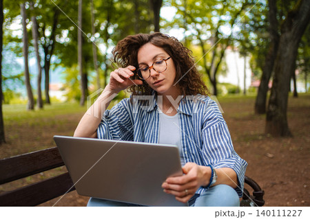 Woman working on laptop outdoors in park with trees 140111227