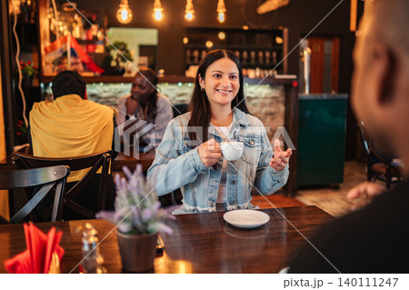 Woman enjoying coffee and conversation with friend in cafe 140111247