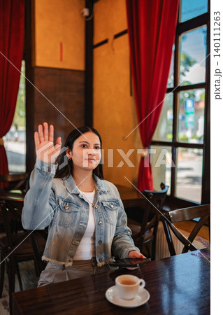 Young adult woman raising hand calling waiter in cafe 140111263
