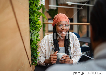 Black woman smiling during coffee meeting in coworking space Black woman smiling during coffee meeting in coworking space 140111325