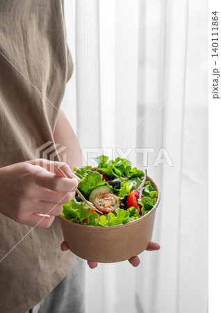A woman holds a healthy vegetable salad in an eco-friendly takeaway bowl. 140111864