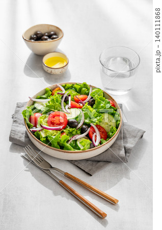 A fresh salad of tomatoes, cucumbers, lettuce, red onions, and olives  on a light background 140111868