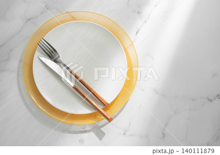 A white and yellow plates with a fork, knife on a marble background A white and yellow plates with a fork, knife on a marble background 140111879