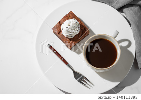 A piece of chocolate brownie with ice cream on a plate and a cup of espresso coffee 140111895