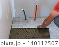 Worker lays tiles in bathroom while adjusting plumbing pipes space is under renovation home 140112507
