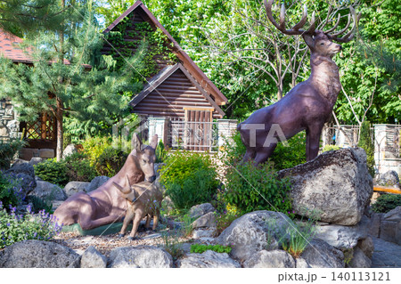 Deer sculptures of a stag, doe and fawn in a landscaped garden beside a rustic wooden cottage Deer sculptures of a stag, doe and fawn in a landscaped garden beside a rustic wooden cottage 140113121
