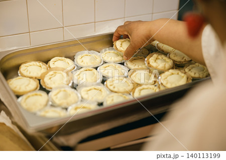 Middle aged Black woman hand arranging handmade tarts in metal tray inside commercial kitchen 140113199
