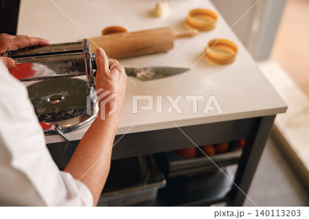 Senior Caucasian woman using a manual pasta machine in a bright domestic kitchen making fresh food 140113203