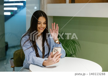 Woman waving during video call using smartphone 140113288