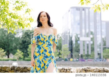 Young woman in summer dress is walking in green park and enjoying the sun. Playful and beautiful girl on warm sunny day. 140113336