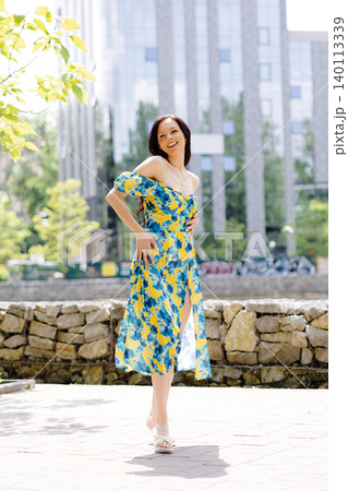 Young woman in summer dress is walking in green park and enjoying the sun. Playful and beautiful girl on warm sunny day. 140113339