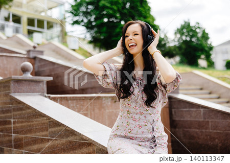 Dancing girl feeling happy in city.Young woman dancing and listening music in headphones, standing on the stairs in park Dancing girl feeling happy in city.Young woman dancing and listening music in headphones, standing on the stairs in park 140113347