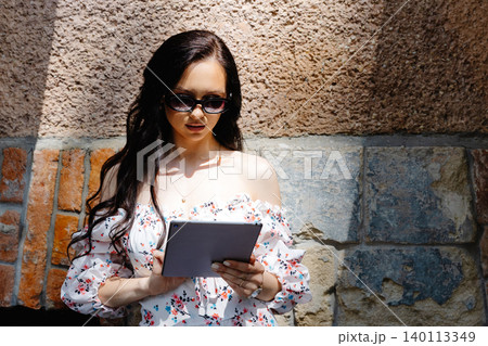 Young woman in sunglasses holding digital tablet in front of brick wall 140113349