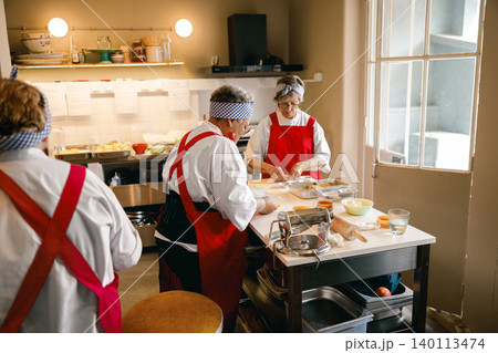 Three senior Caucasian women preparing fresh dough for pastries in a kitchen Three senior Caucasian women preparing fresh dough for pastries in a kitchen 140113474