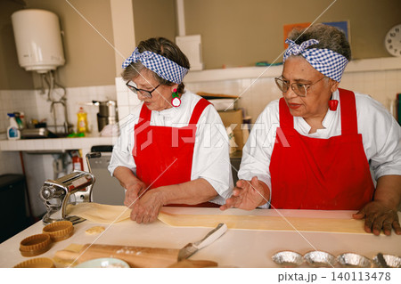 Caucasian and Hispanic senior women making fresh pasta dough in a bright community kitchen space Caucasian and Hispanic senior women making fresh pasta dough in a bright community kitchen space 140113478