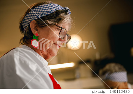 Active senior Caucasian woman cooking in a professional kitchen with authentic vitality 140113480