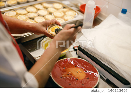Middle aged Asian woman brushing egg wash on pastry tarts in a busy commercial bakery kitchen Middle aged Asian woman brushing egg wash on pastry tarts in a busy commercial bakery kitchen 140113495